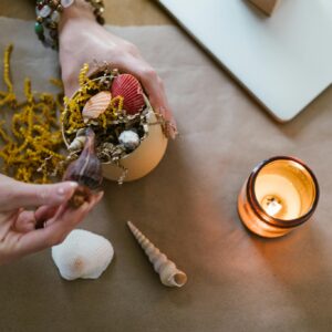 A cozy scene of hands crafting with seashells and candlelight.