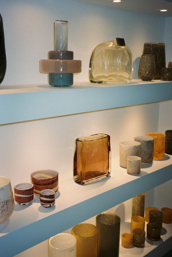 A well-lit arrangement of diverse ceramic and glass vases on shelves.